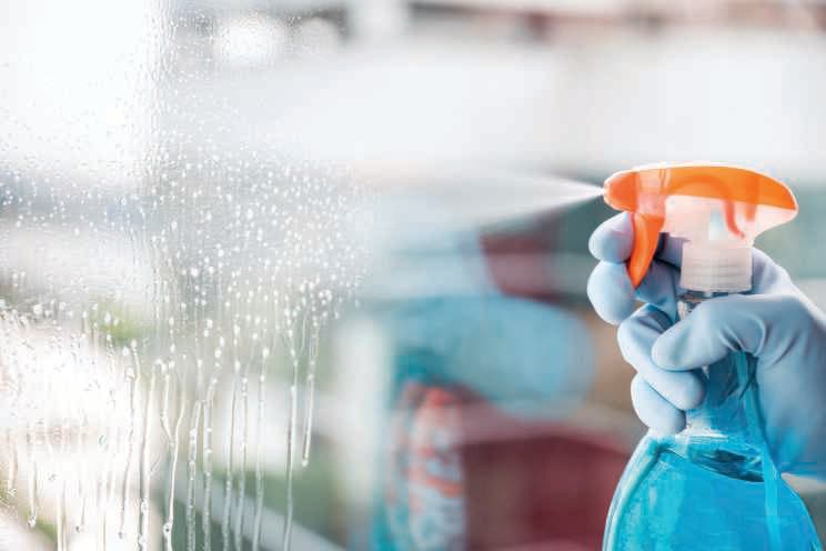 Gloved hand spraying cleaning solution on glass